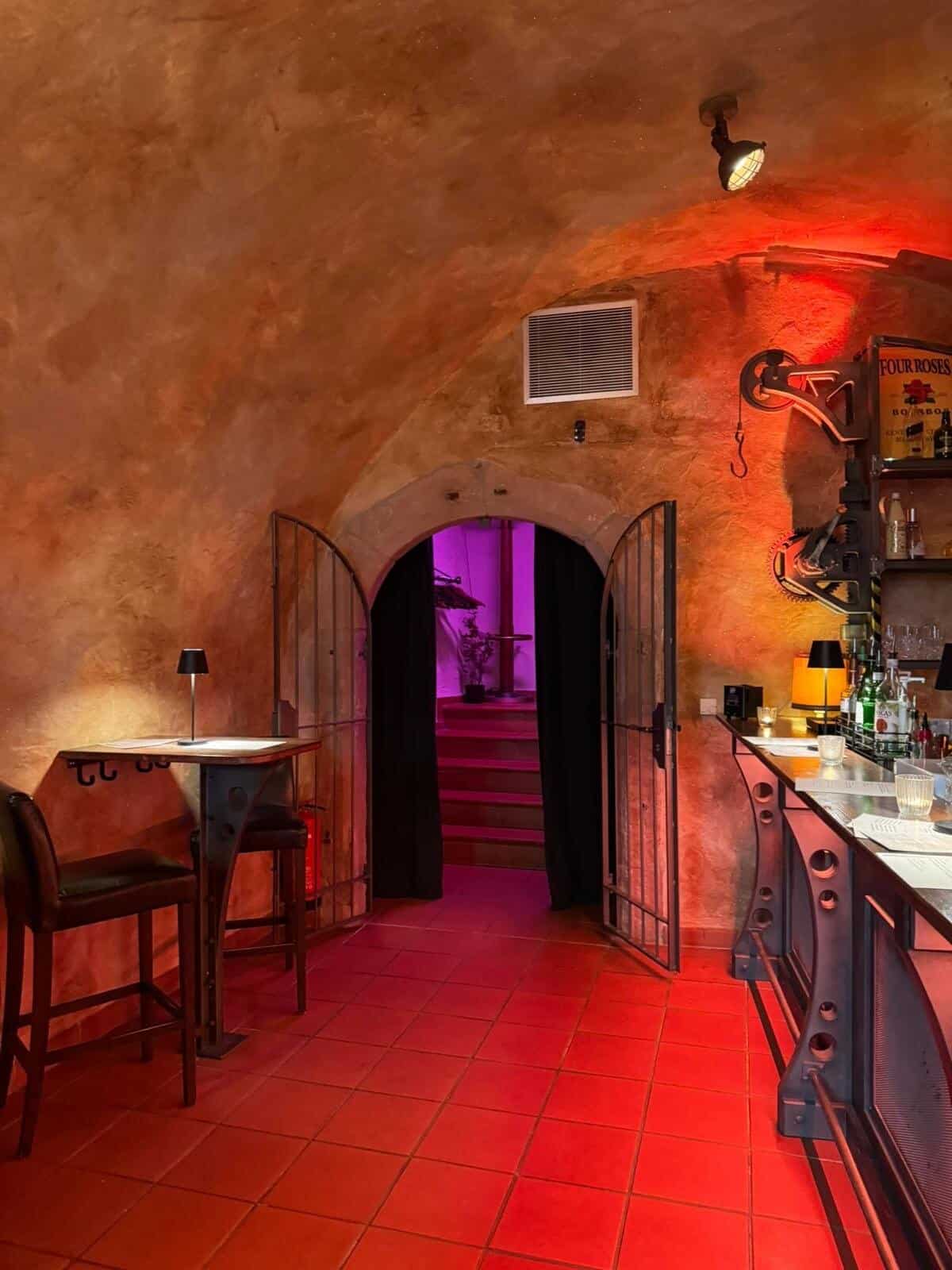 Stimmungsvoller Eingang zum Gewölbekeller der D48 Bar mit schmiedeeisernem Tor und roter Beleuchtung